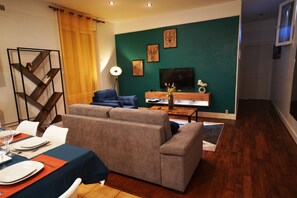 A modern living room with a sofa, a dining table set for four, and a TV mounted on the wall.