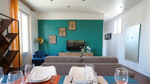 Spiseområde med et bord dækket til fire personer, en sofa i baggrunden og en væg i teal farve.