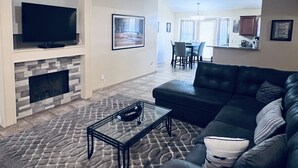 A living room with a stone fireplace, a black leather sofa, and a glass coffee table. - Pool home in Phoenix Retreat close to everything! (Phoenix)
