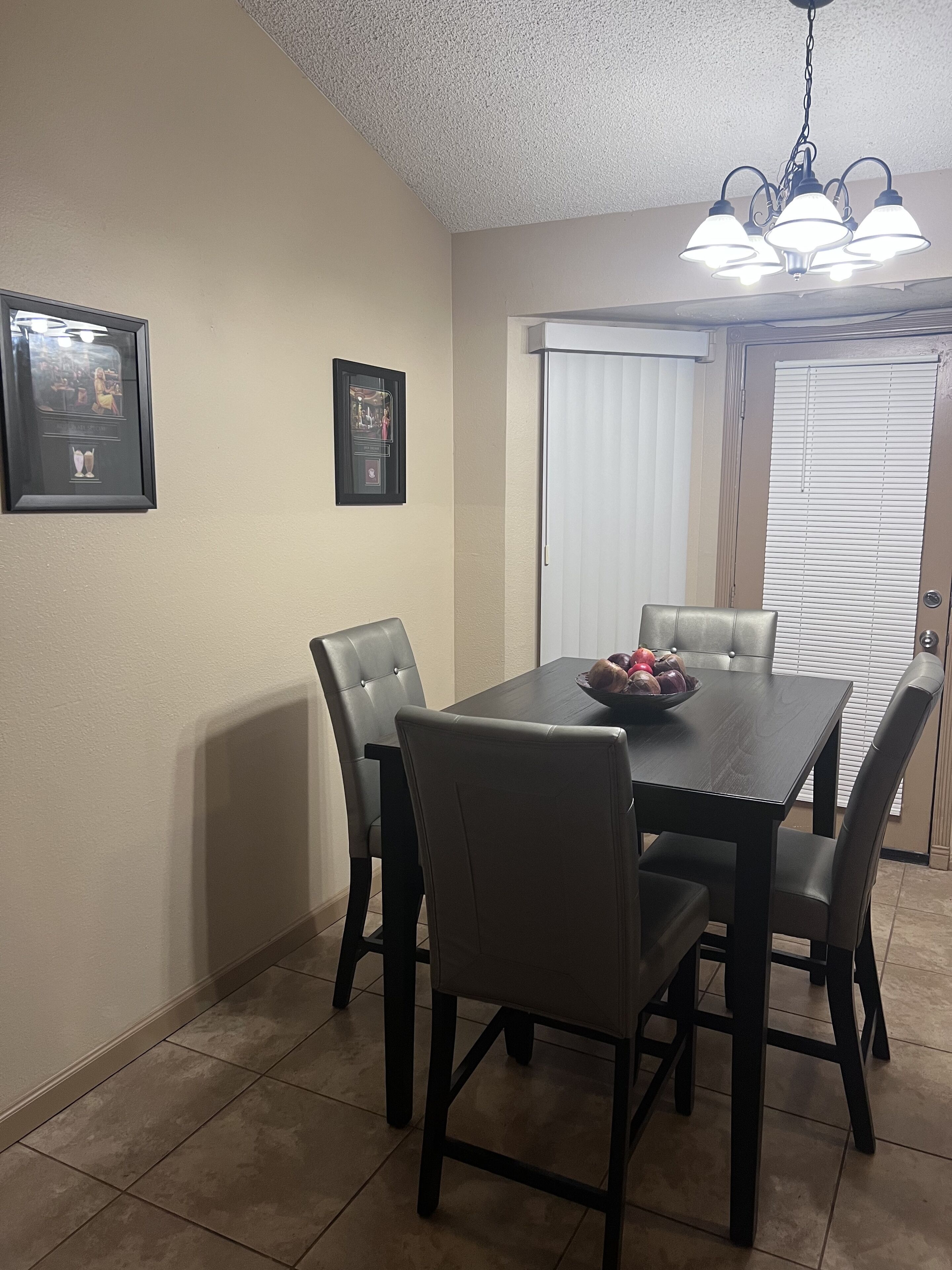A dining area with a dark wooden table, six chairs, and a chandelier. There are two framed pictures on the wall.