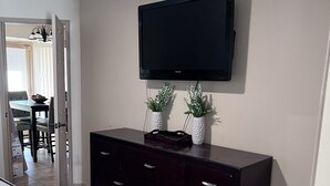 A bedroom with a bed, a dark wooden dresser, a flat-screen TV mounted on the wall, and two white decorative vases on the dresser. - Pool home in Phoenix Retreat close to everything! (Phoenix)