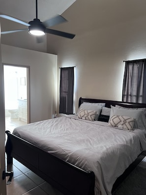 Un dormitorio con cama, ventilador de techo y ventana con cortinas.