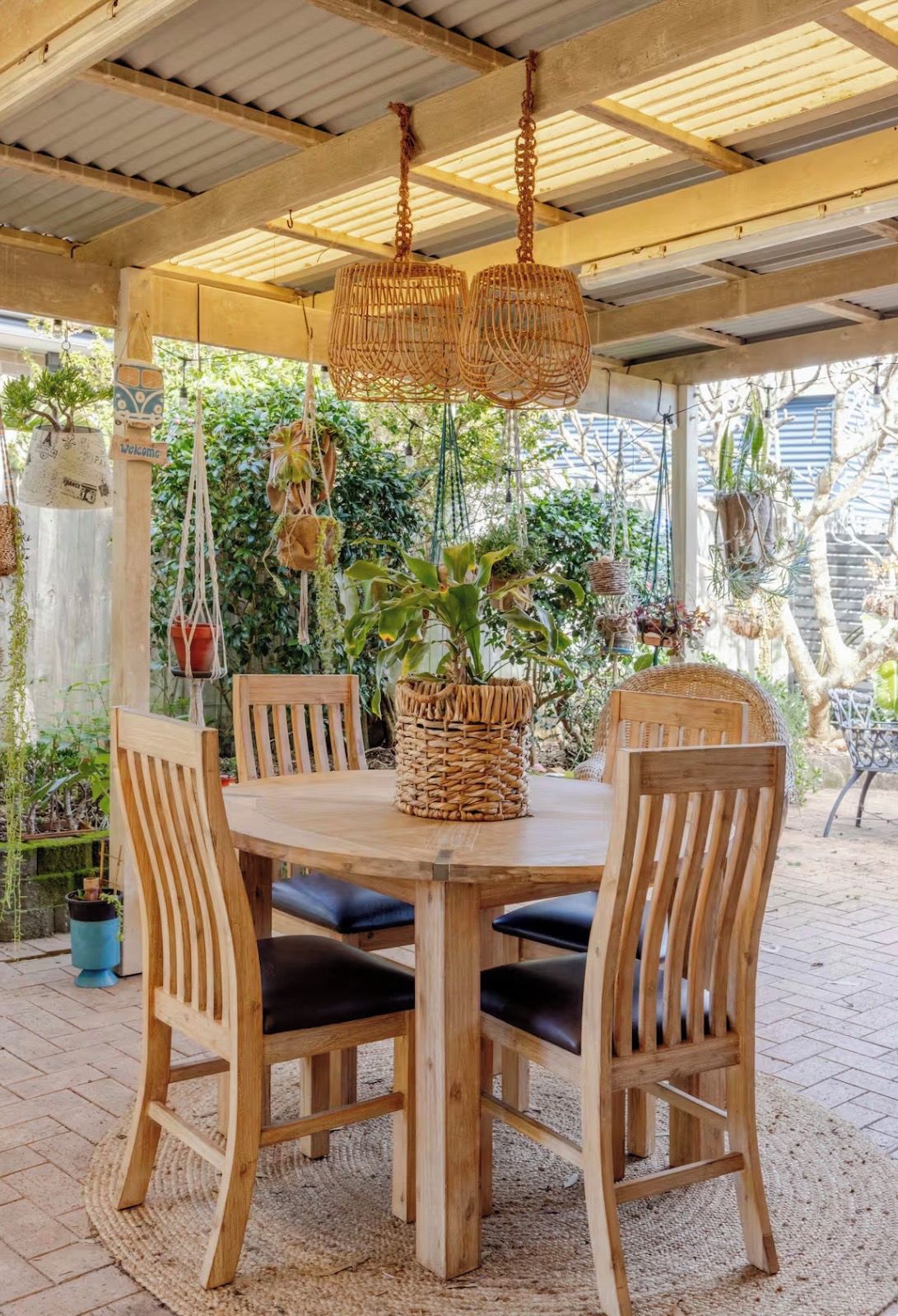 An outdoor wooden table with four chairs, a woven basket centerpiece, and hanging wicker lamps.
