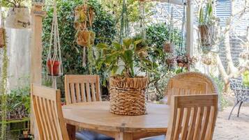An outdoor wooden table with four chairs, a woven basket centerpiece, and hanging wicker lamps.