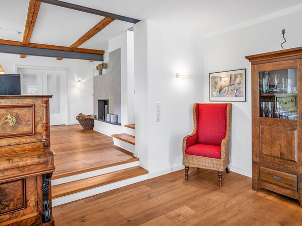 A spacious living room with hardwood floors, a red upholstered chair, a wooden cabinet, and a fireplace.