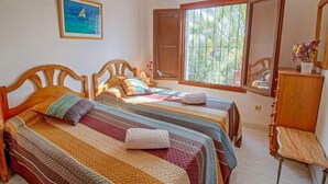 A room with two wooden beds, a wooden chair, a window with a view of palm trees, and an air conditioning unit. - Shangrila by Interhome (Calpe/Calp)