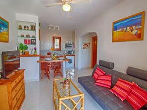 Uma sala de estar moderna com sofá, TV e um espaço de jantar com cadeiras e mesa.