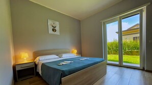 Un dormitorio con cama, mesitas de noche, una lámpara y vistas a través de un ventanal corredera.