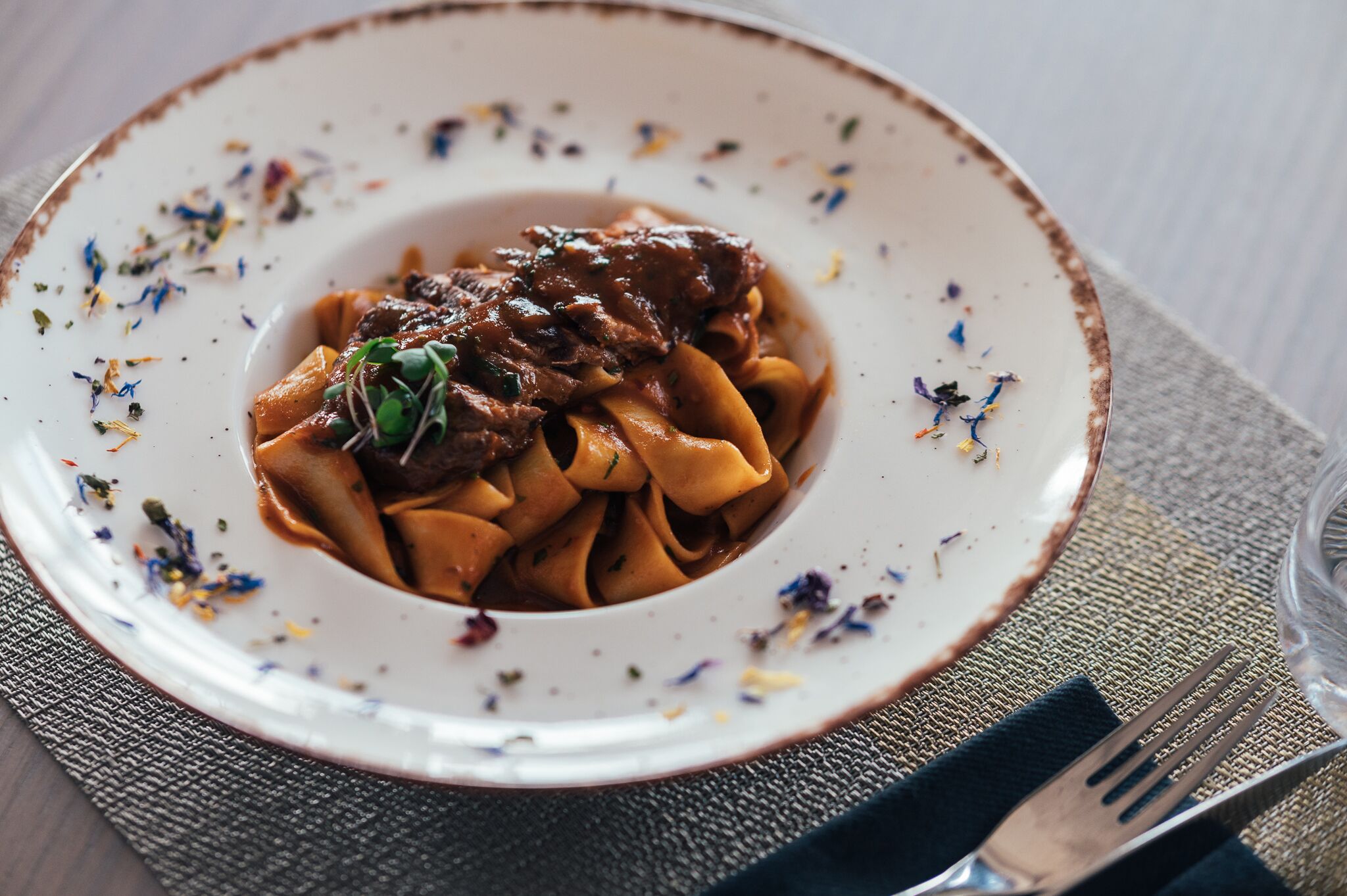 A plate of pasta with a brown sauce and garnished with herbs, placed on a textured placemat.