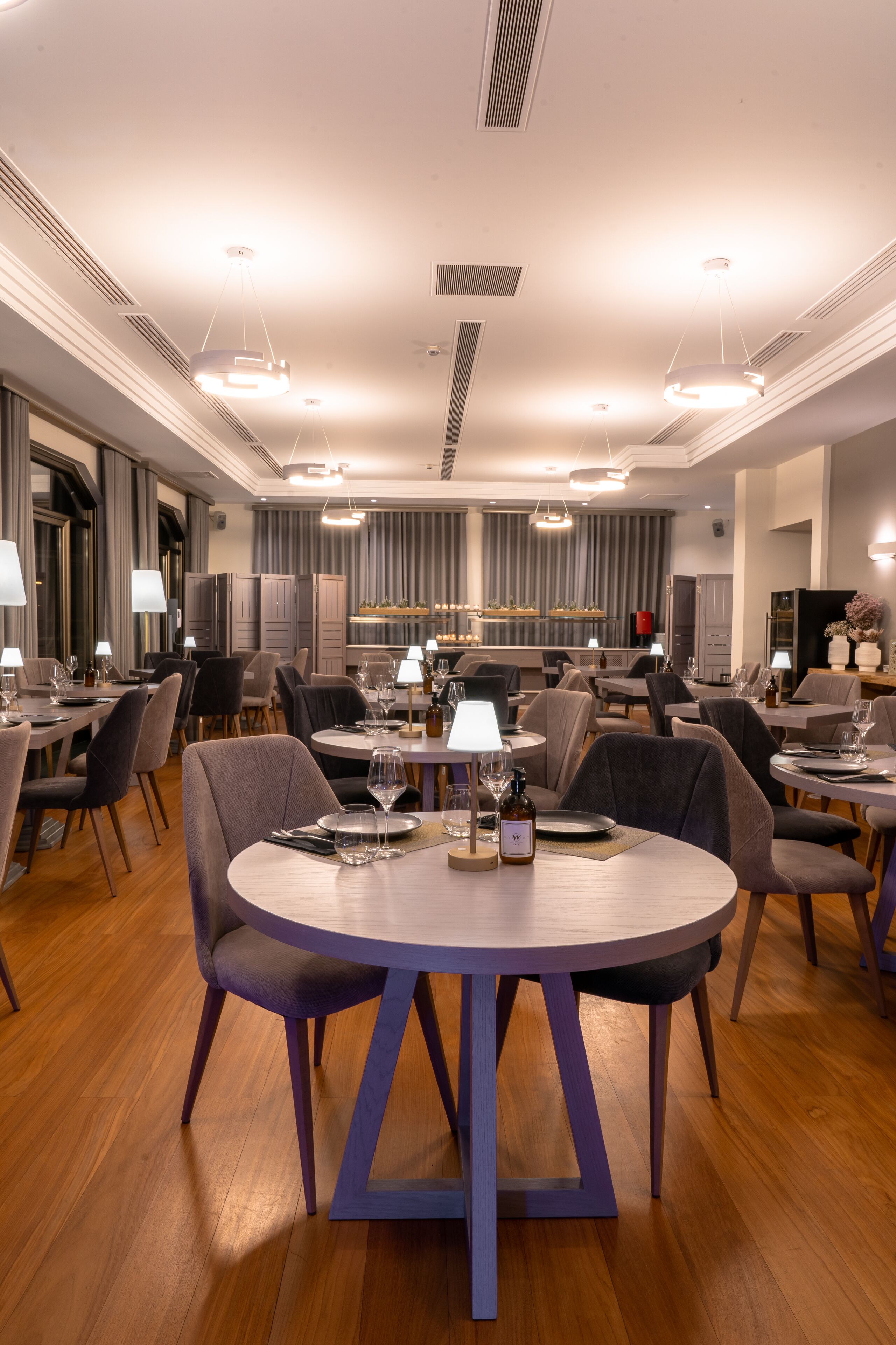 A modern dining area with round tables, chairs, and overhead lighting.