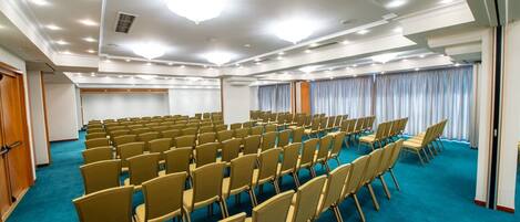 Un salón de conferencias con filas de sillas, alfombra azul y techo blanco con iluminación empotrada.