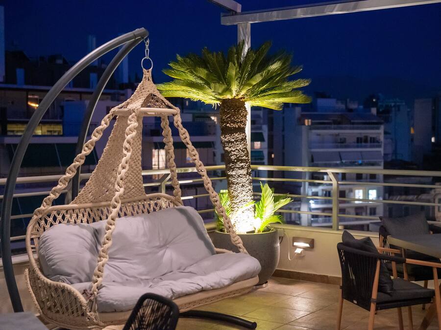 A balcony with a hanging chair, a table, and a potted palm tree.