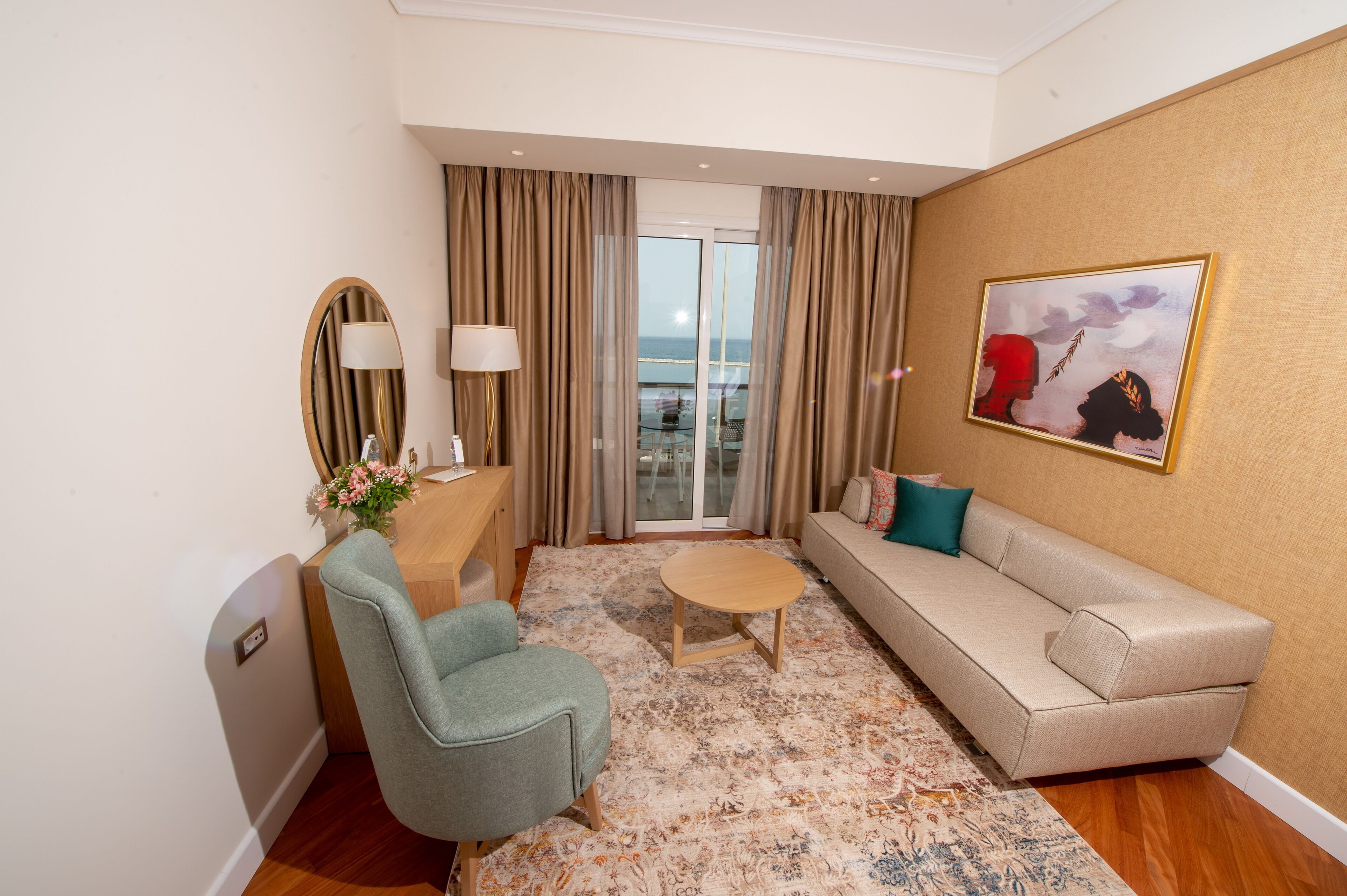 A hotel room with a sofa, armchair, coffee table, and a painting on the wall.