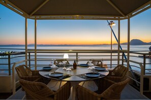 A dining area with a table set for four, overlooking a body of water and distant mountains at sunset. - MY WAY HOTEL & EVENTS (Patras)