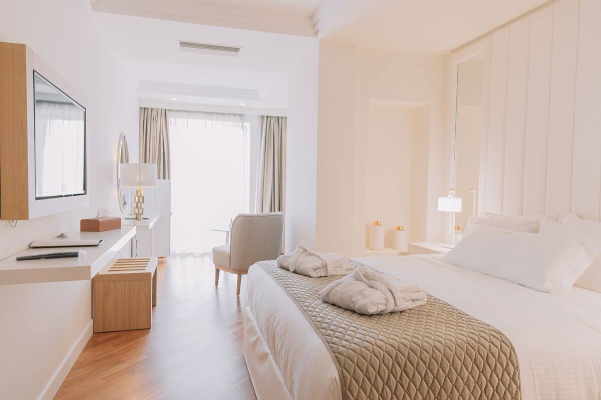 A hotel room with a bed, a desk, a chair, a mirror, and a window with curtains.