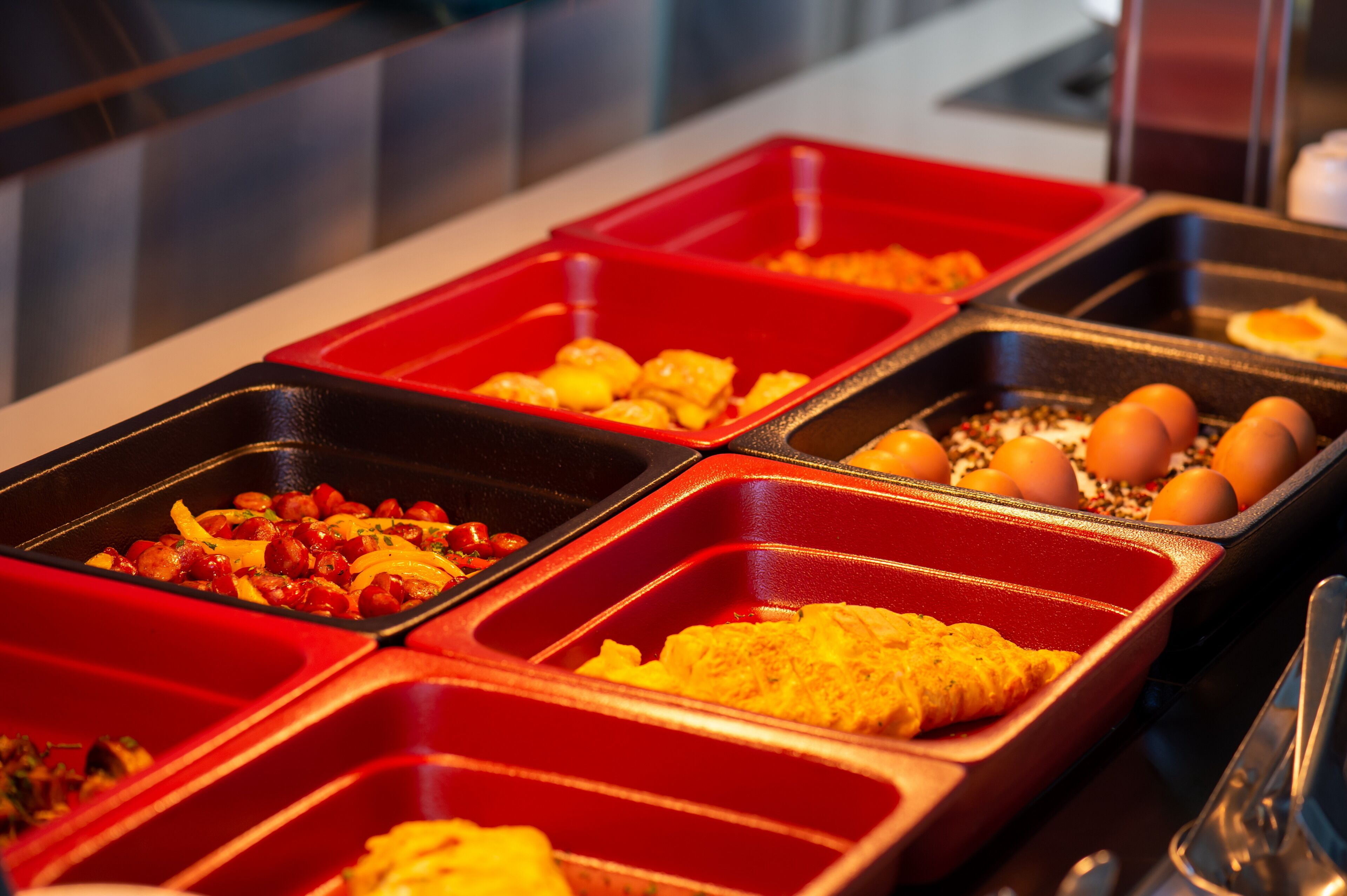 Un bufé con diferentes alimentos en bandejas rojas y negras.
