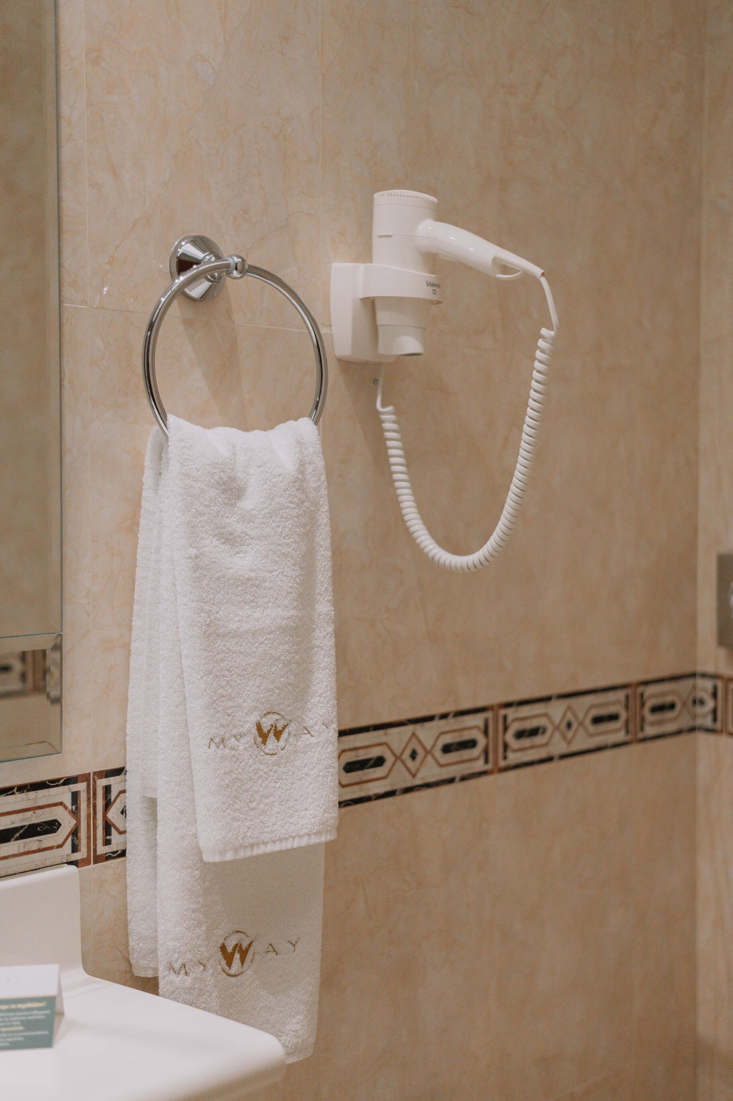 A bathroom with a towel rack holding two white towels, a handheld showerhead, and a decorative tile border.
