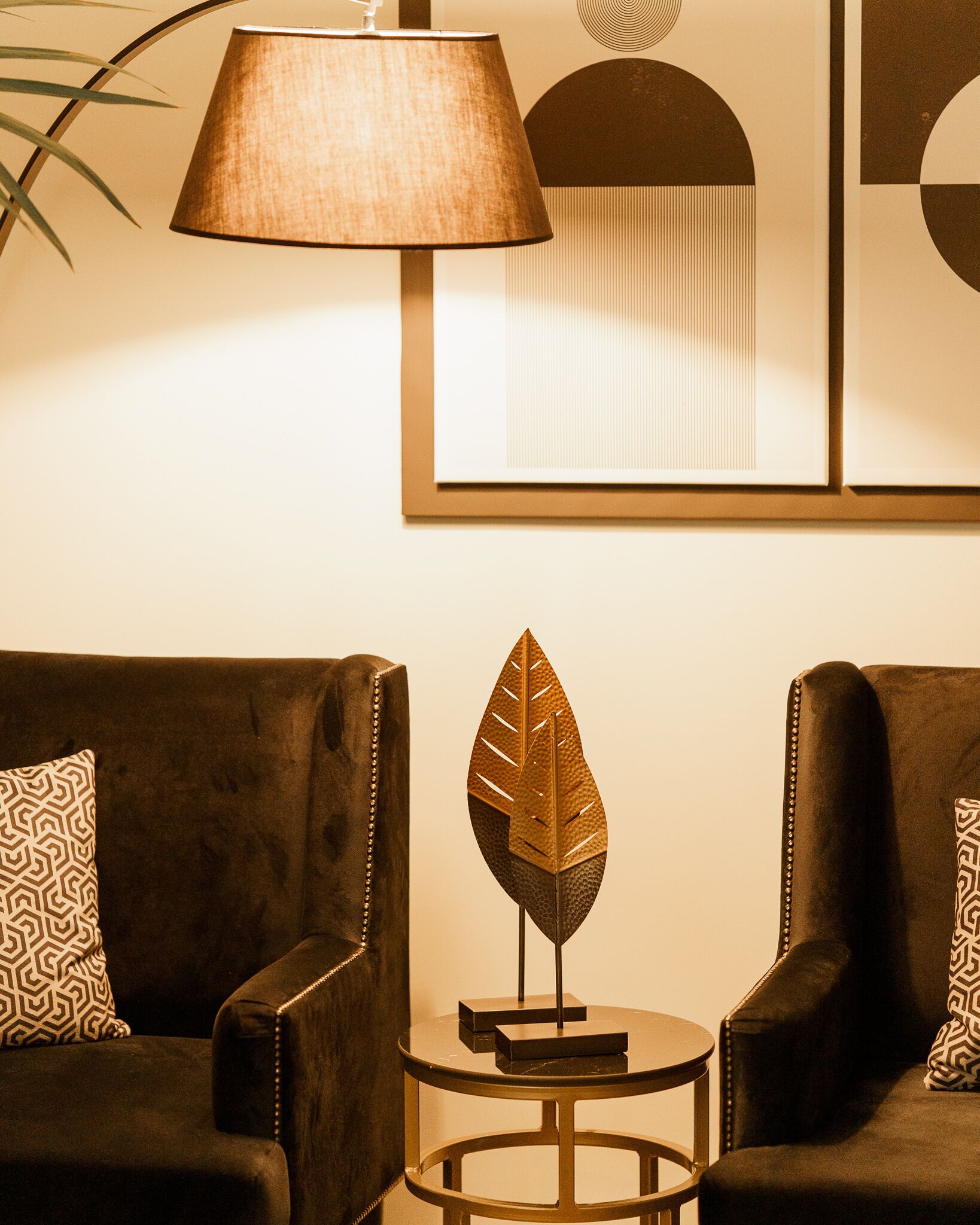 Una sala de estar moderna con dos sofás oscuros, una mesita redonda, una escultura decorativa de hoja y una lámpara de pared.