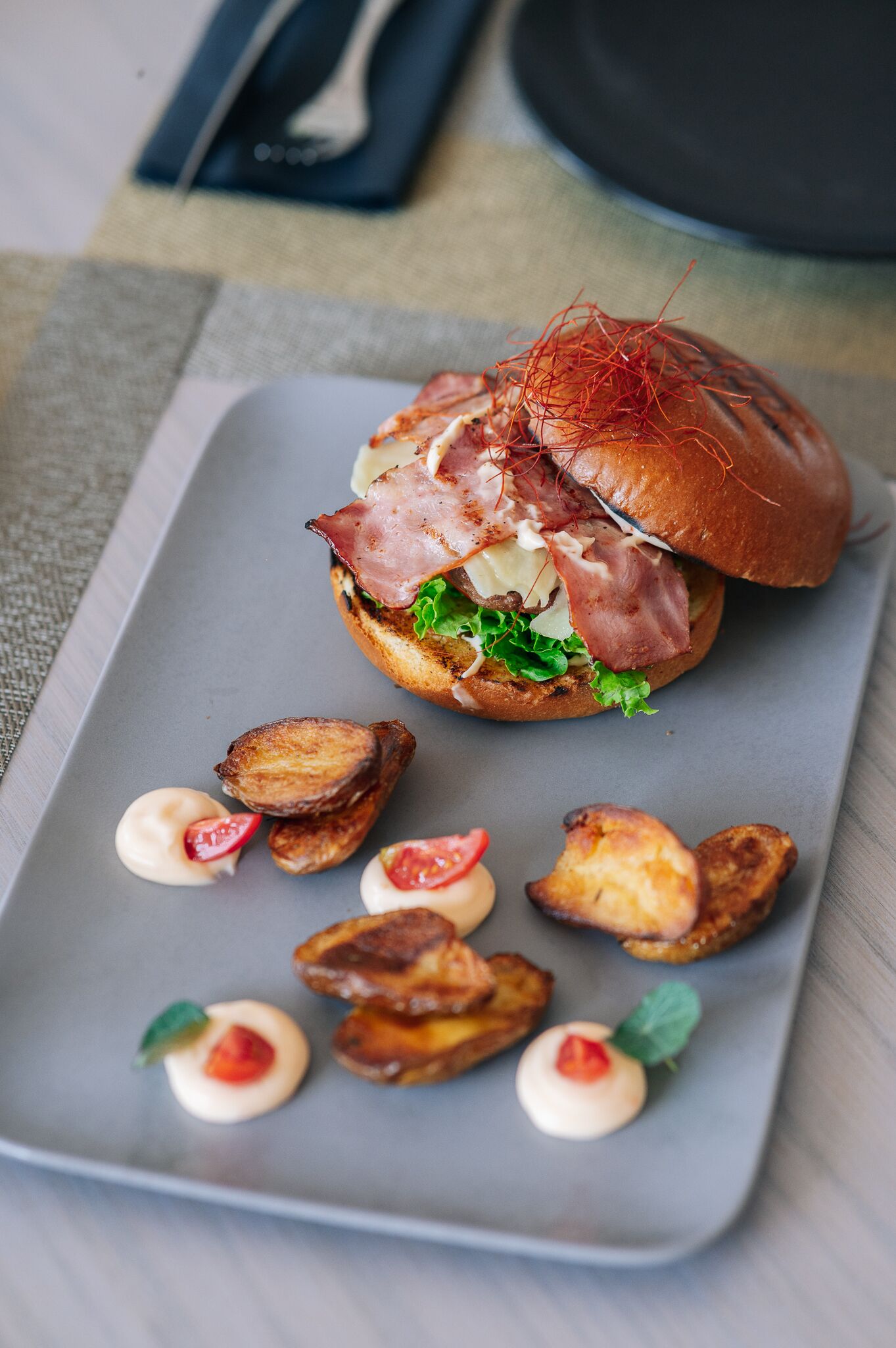 A plate with a sandwich, roasted potatoes, and small dollops of sauce.