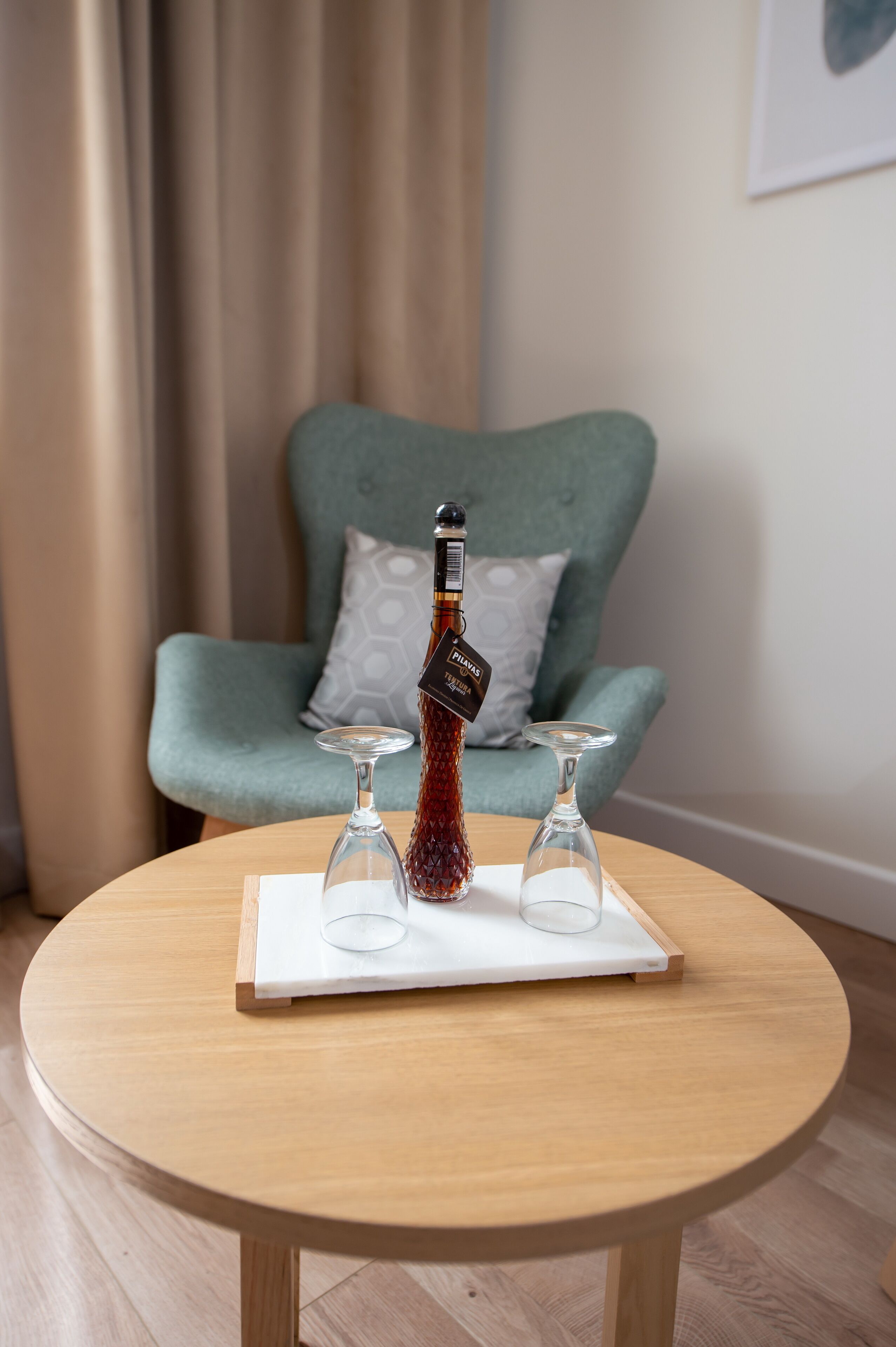 A round wooden table with a bottle of wine and three wine glasses on a white tray.