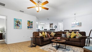 A living room with a brown sectional sofa, a ceiling fan, and a dining area in the background. -  A-POP of Sunshine  (Davenport)