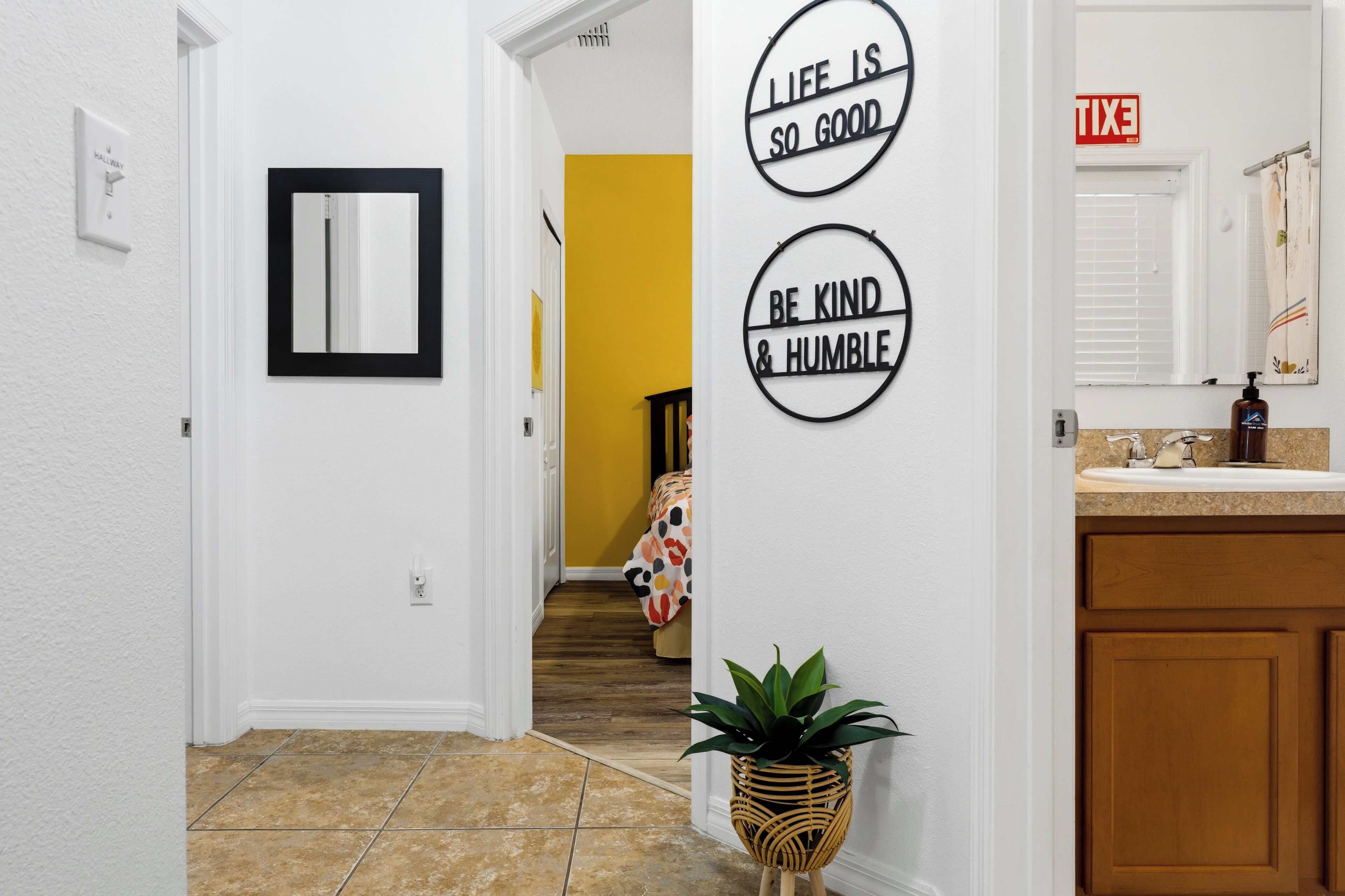A hallway with a mirror, a potted plant, and motivational wall art.