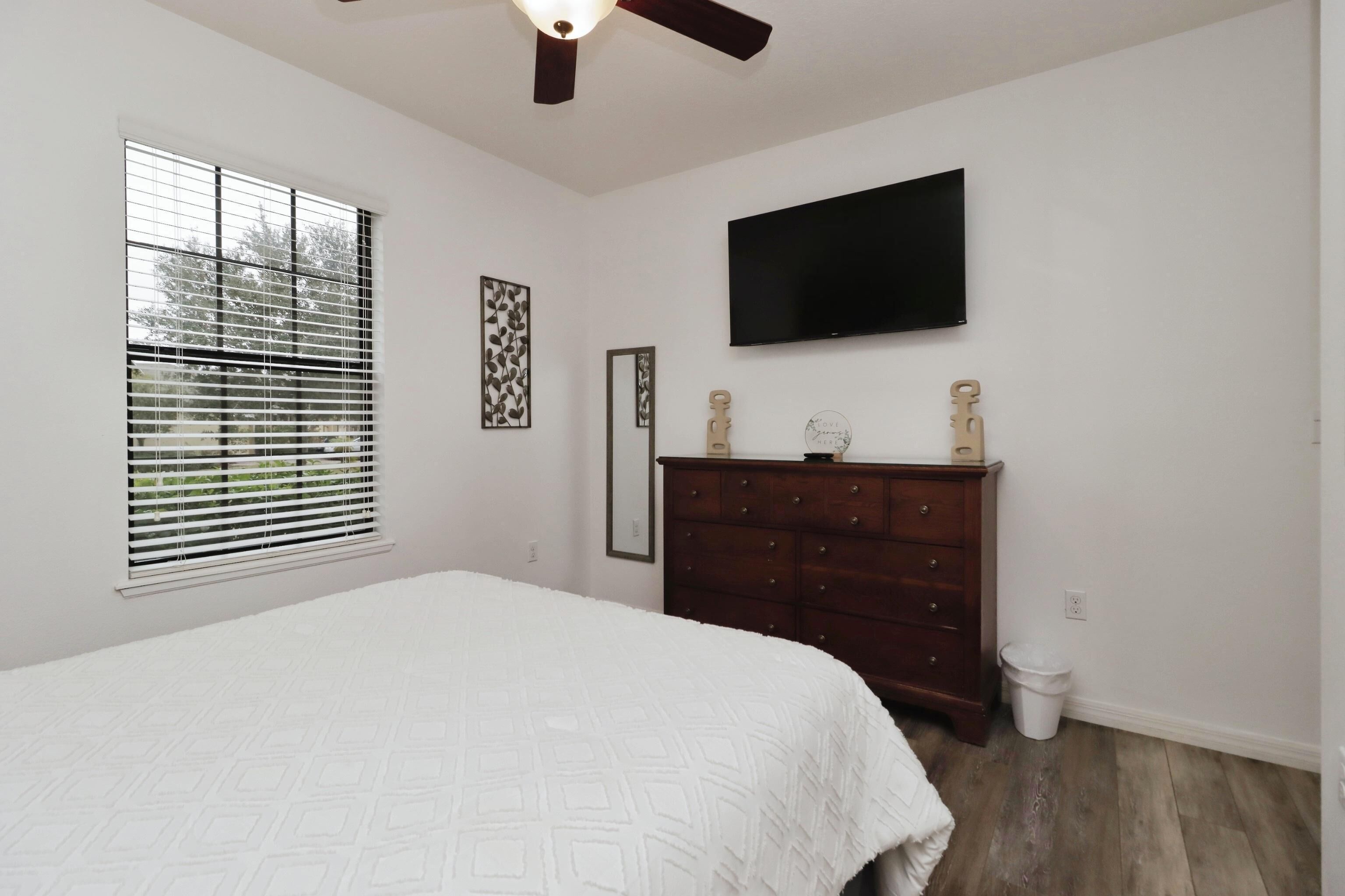 A bedroom with a bed, a dresser, a television, and a window with blinds.