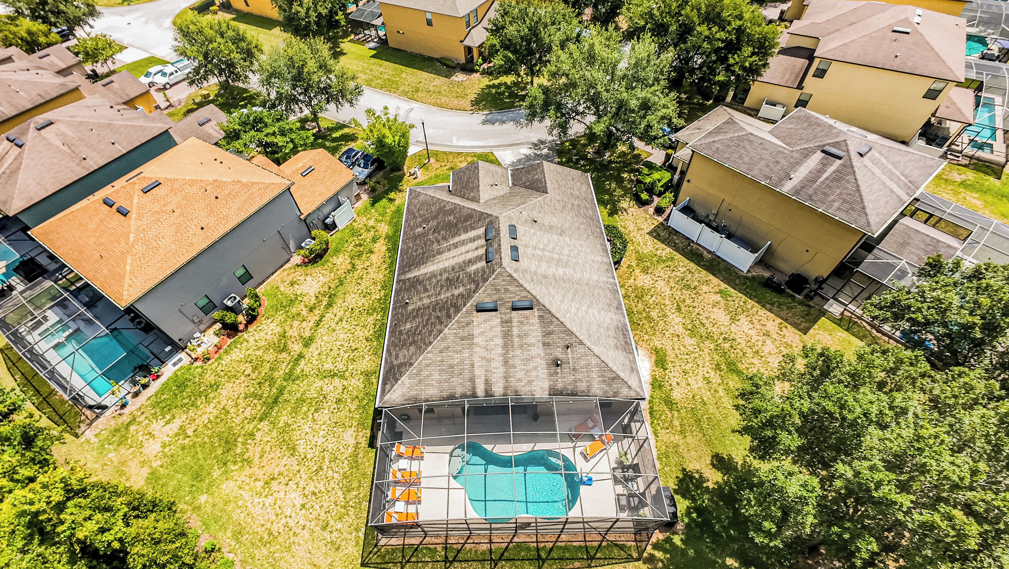 Vista aérea de un vecindario con una casa que tiene piscina en la azotea, rodeada de otras casas y vegetación.