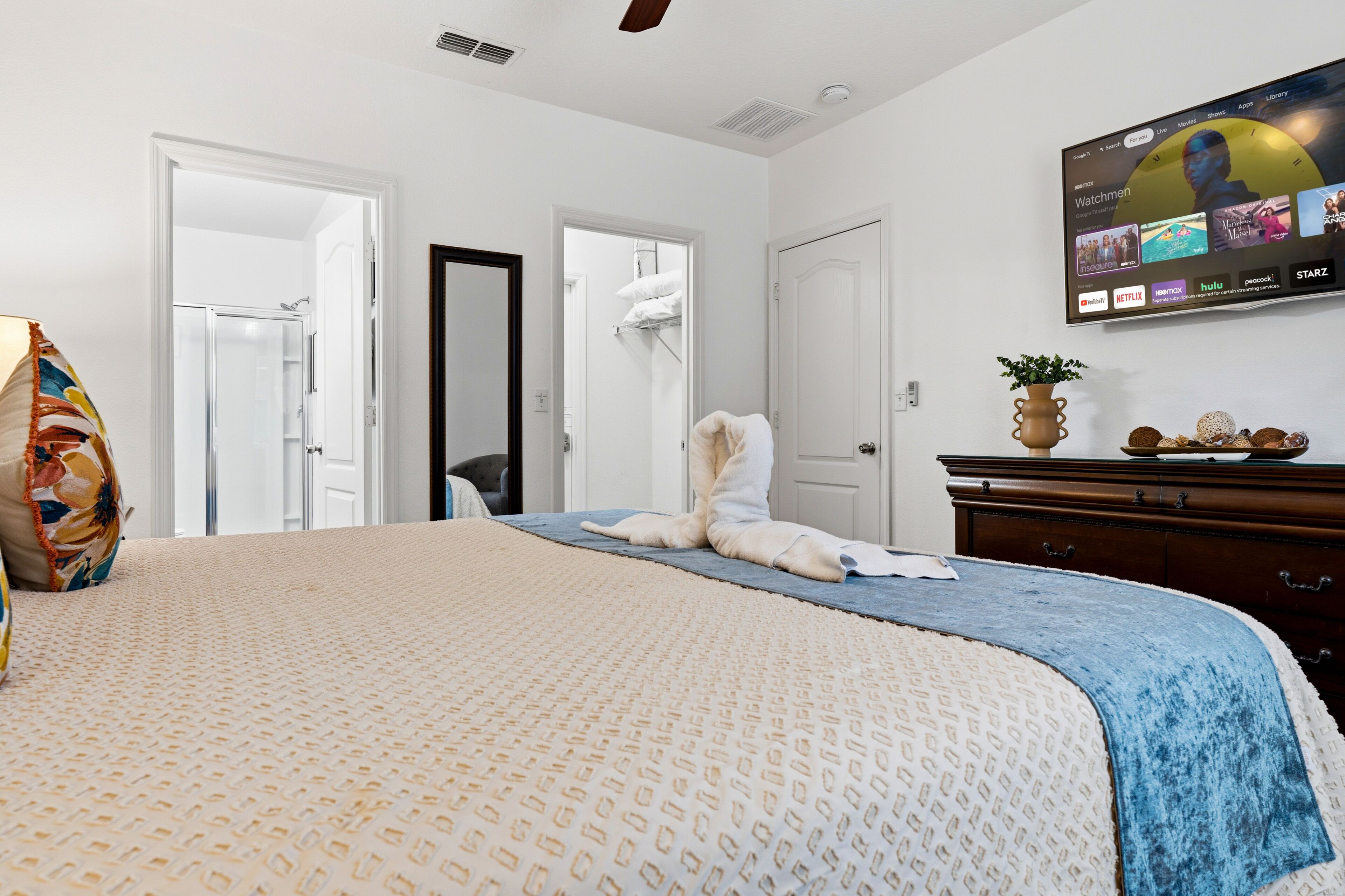 A hotel room with a bed, a TV mounted on the wall, a dresser, and a door leading to a bathroom.