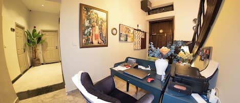 A home office with a desk, computer, and chair. There is a large painting on the wall, a calendar, and a mirror.