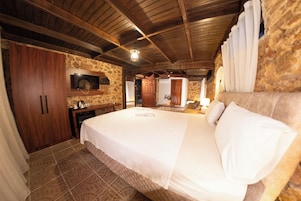 A bedroom with a large bed, wooden wardrobe, stone walls, and a television mounted on the wall.