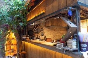 A rustic kitchen with wooden shelves, a hanging pot rack, and various kitchen utensils.