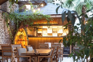 An outdoor seating area with wooden tables and chairs, a sign reading "Maria Lounge," and a menu board visible in the background.