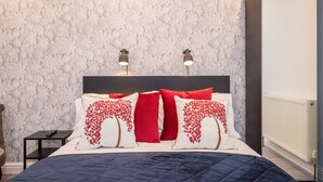 A neatly made bed with a blue quilt, red and white pillows, and two bedside lamps.