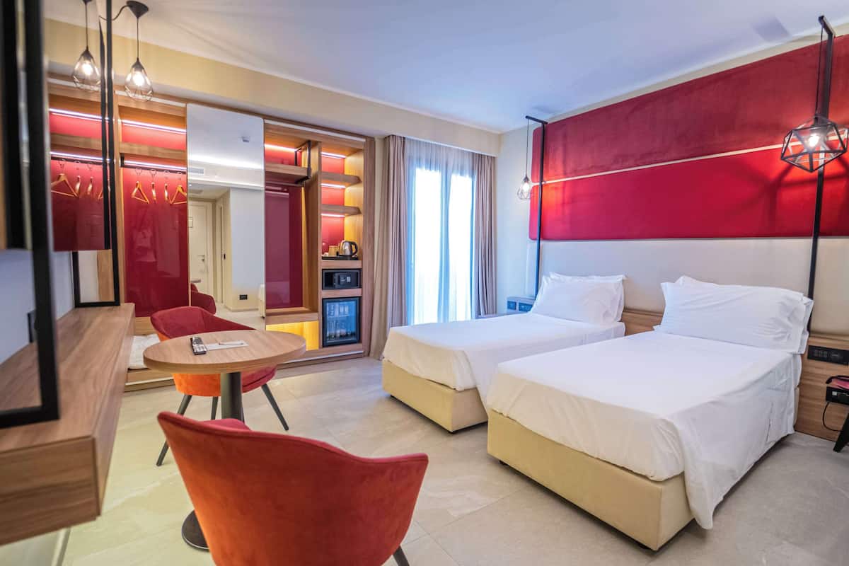 A hotel room with two beds, a dining area with a table and chairs, and a mirror reflecting the room.