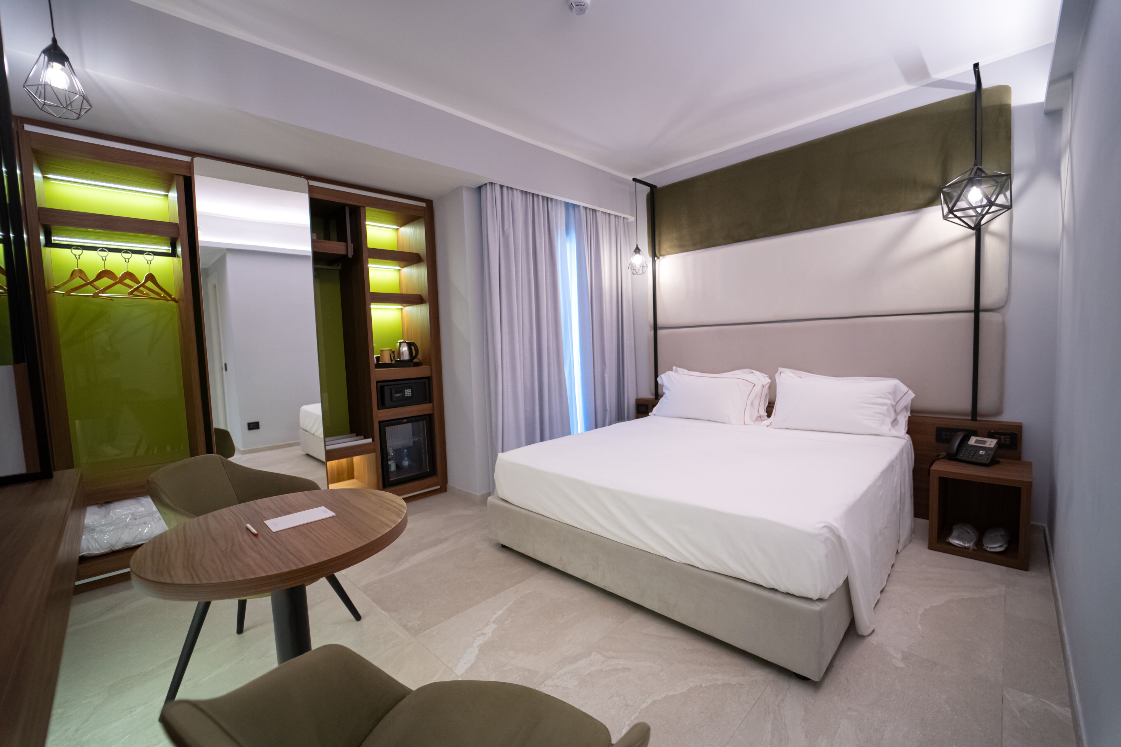 Una habitación de hotel moderna con una cama grande, un escritorio con una silla, un armario y una mesita.