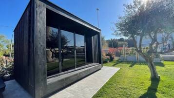 A modern, dark-colored building with large windows, a paved patio, and a well-maintained lawn.
