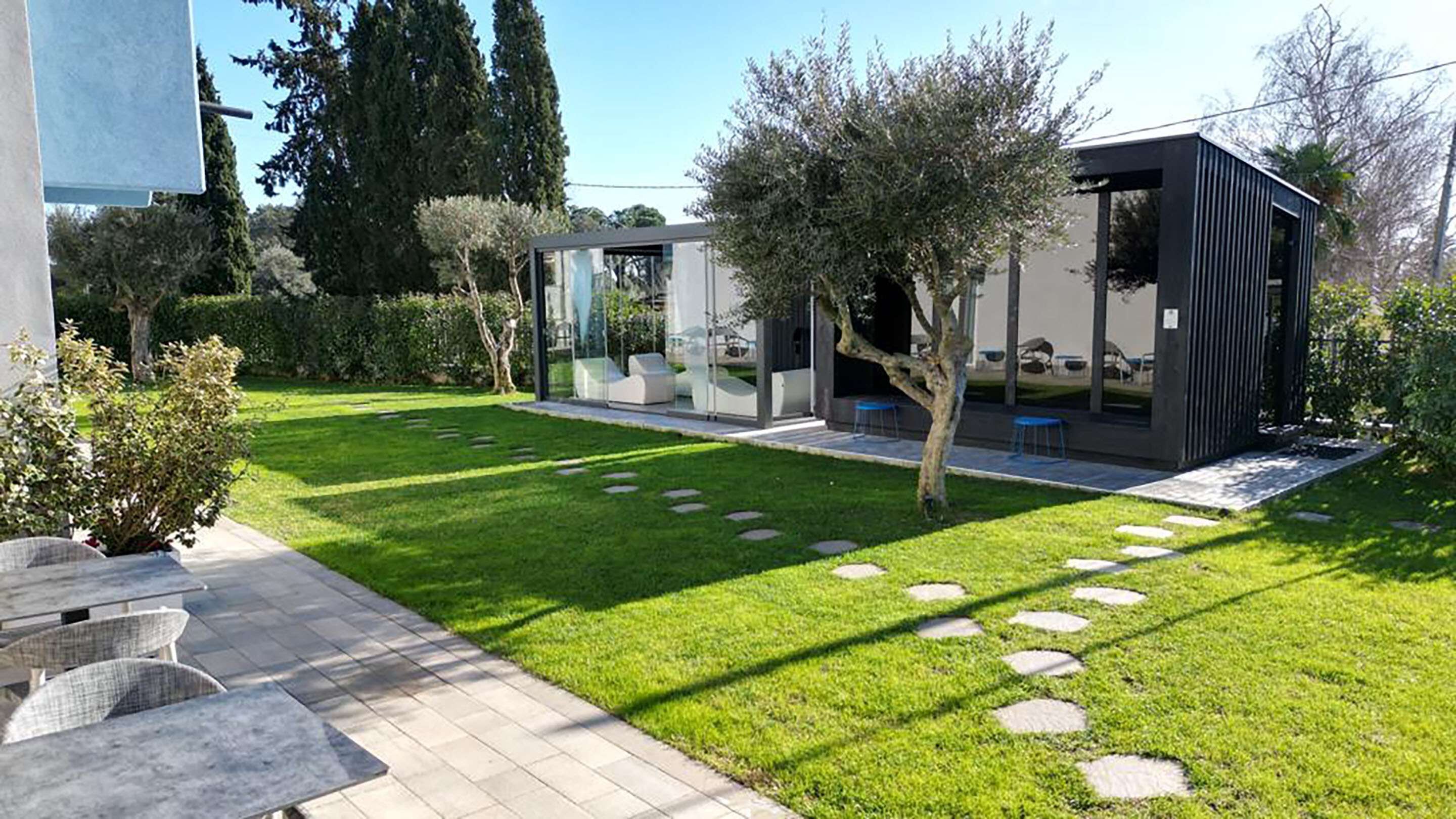 Un patio exterior moderno con césped bien cuidado, piedras para caminar y mobiliario de exterior.