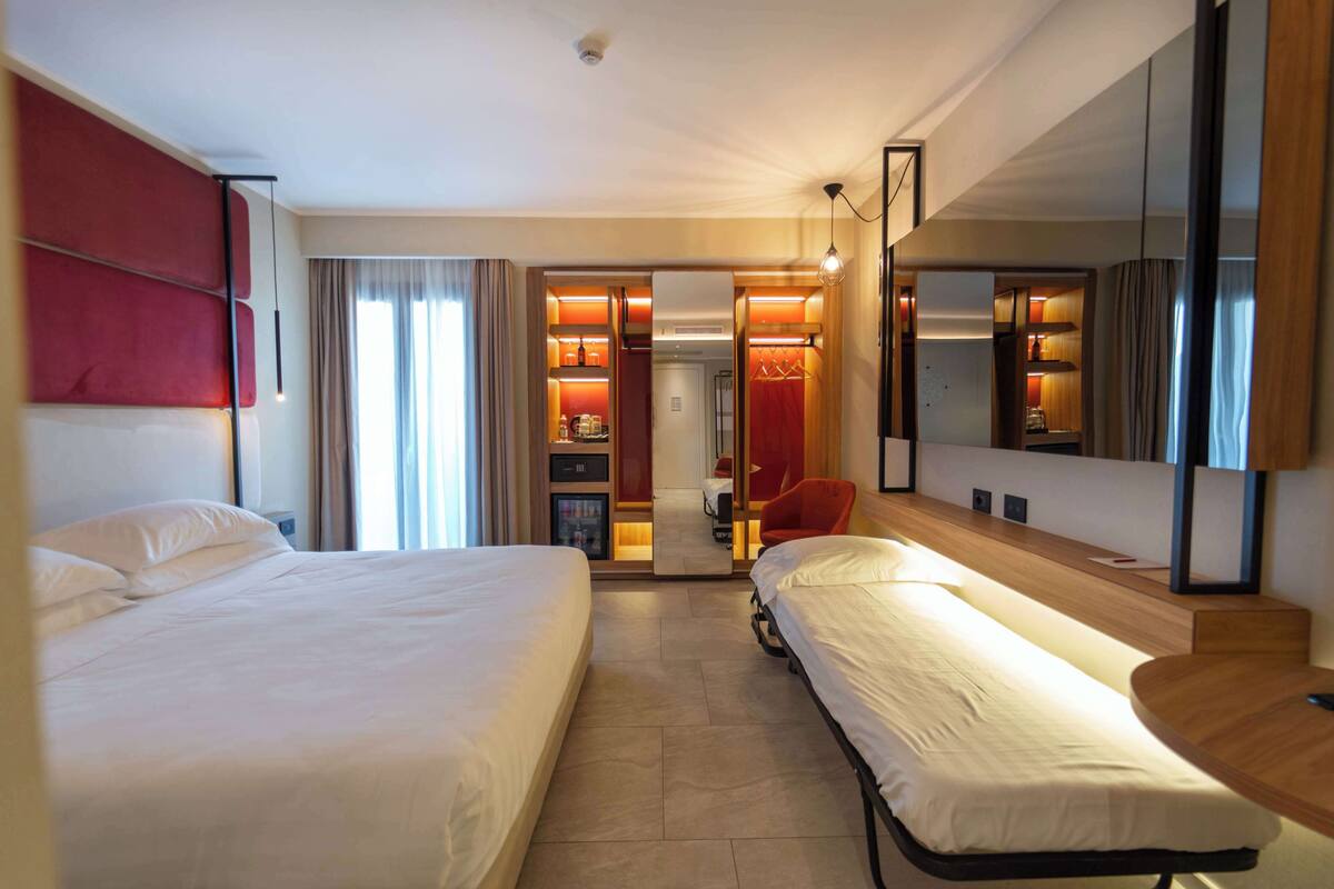 A hotel room with two beds, a wardrobe, a mirror, and a small desk.