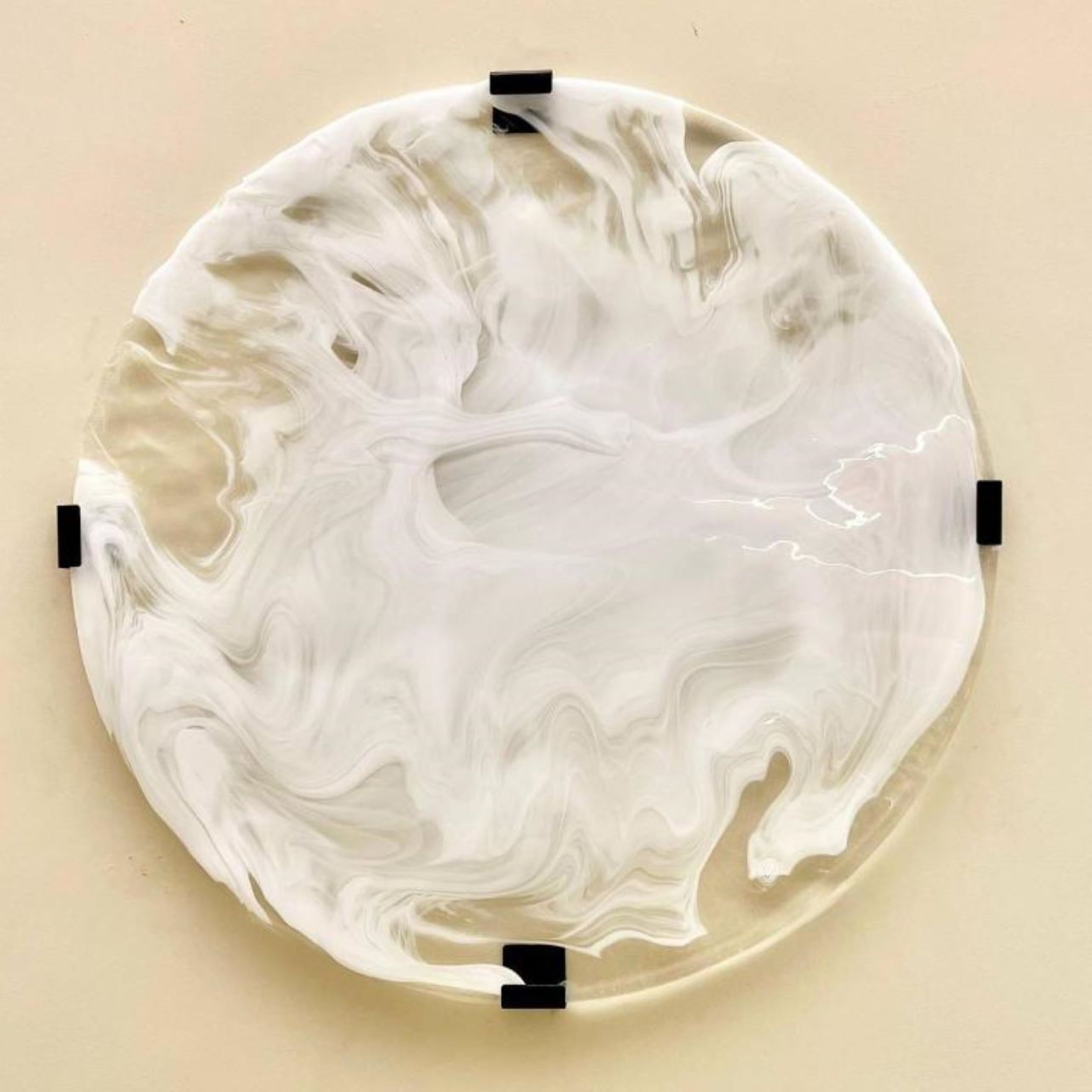 Una pieza artística de vidrio circular con un patrón ondulante, fijada a la pared.