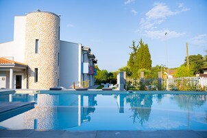Una piscina con muros de piedra, un cielo azul despejado y un jardín cercado.