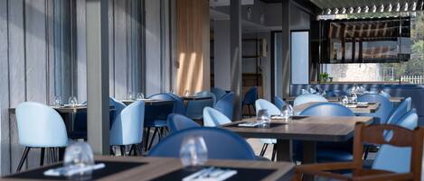 A modern restaurant with blue chairs, wooden tables, and a view of the outdoors.