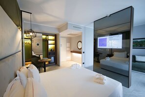 A modern hotel room with a large bed, a desk, a chair, and a TV displaying a map.