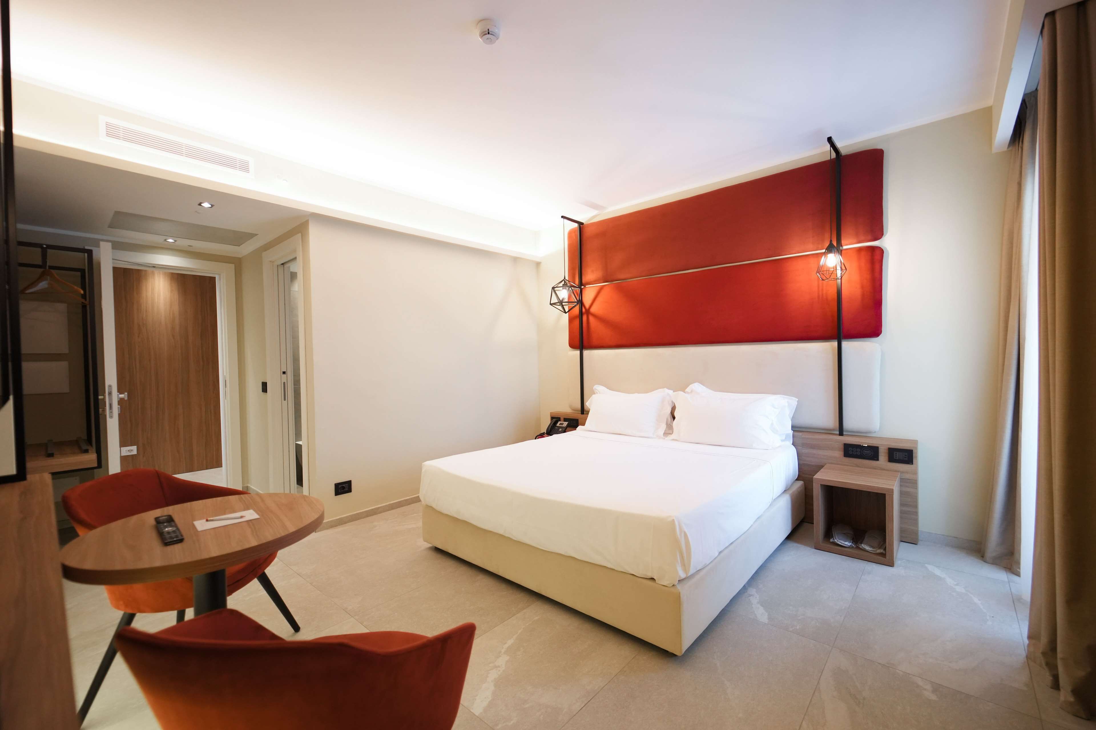 A hotel room with a large bed, a bedside table, a chair, and a small table.