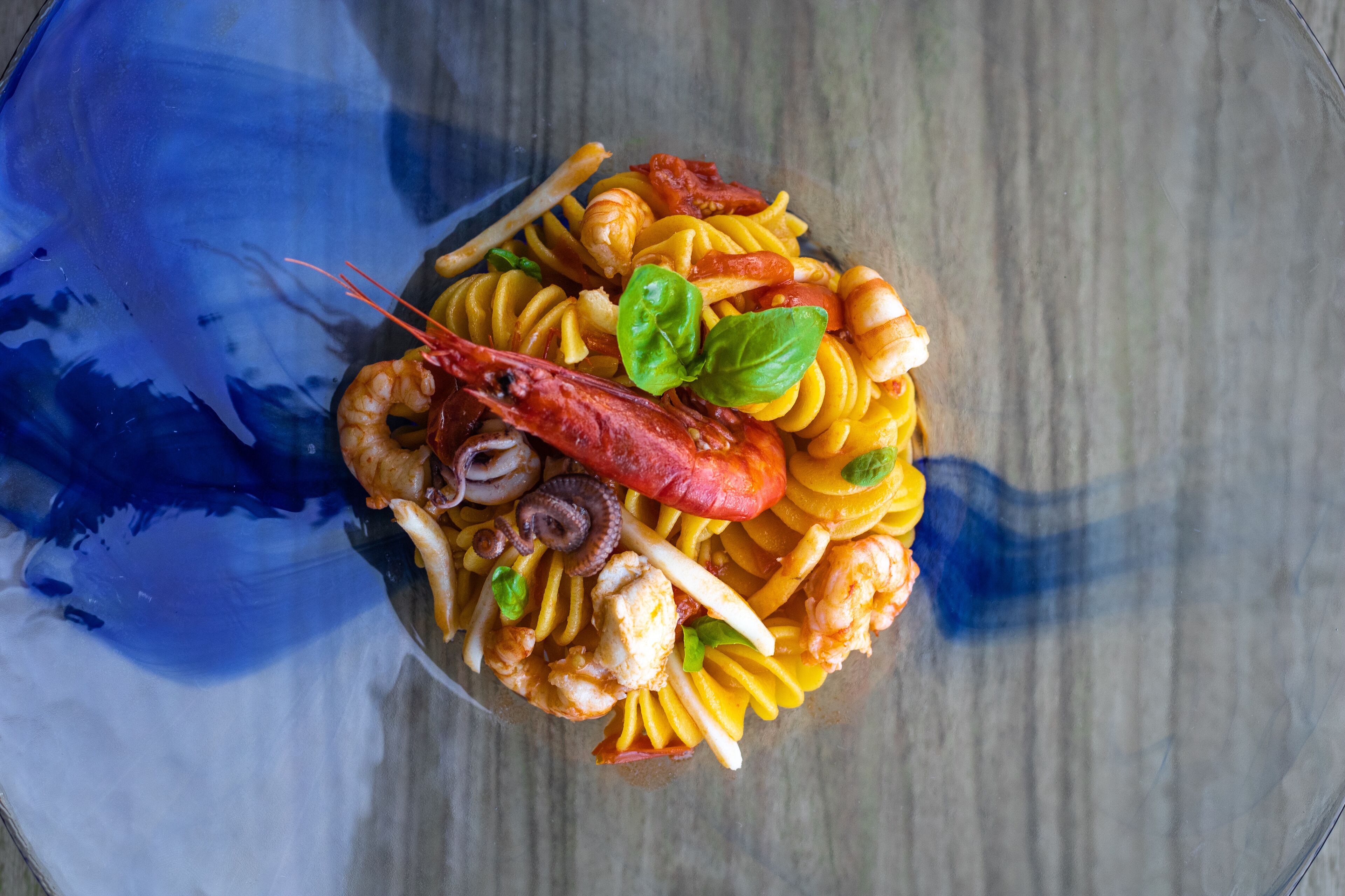 Een pastagerecht met zeevruchten, garnalen, inktvis en basilicum, geserveerd op een glazen bord.