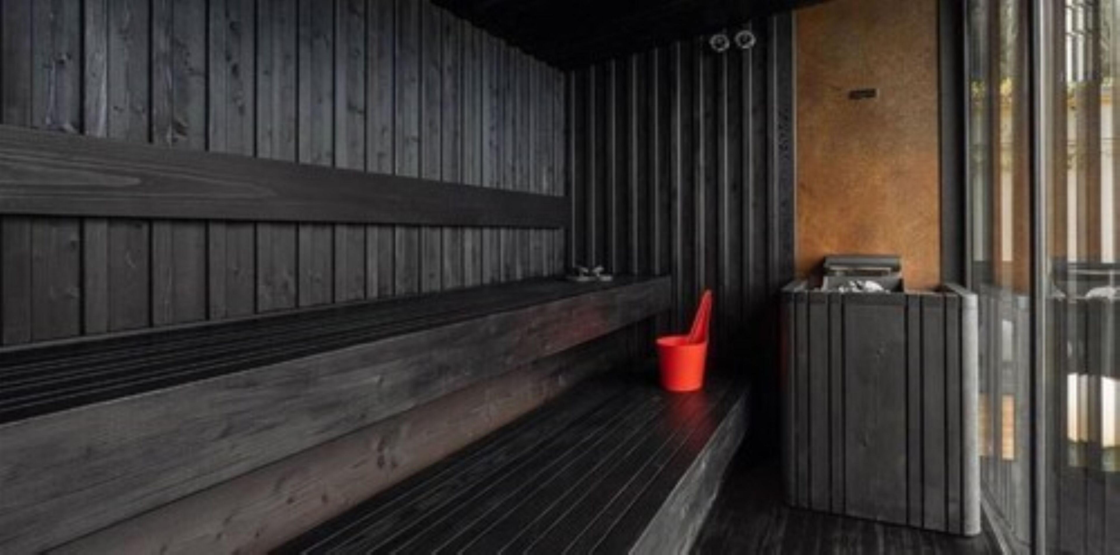 A wooden bench with a red bucket and a trash bin in a modern interior space.