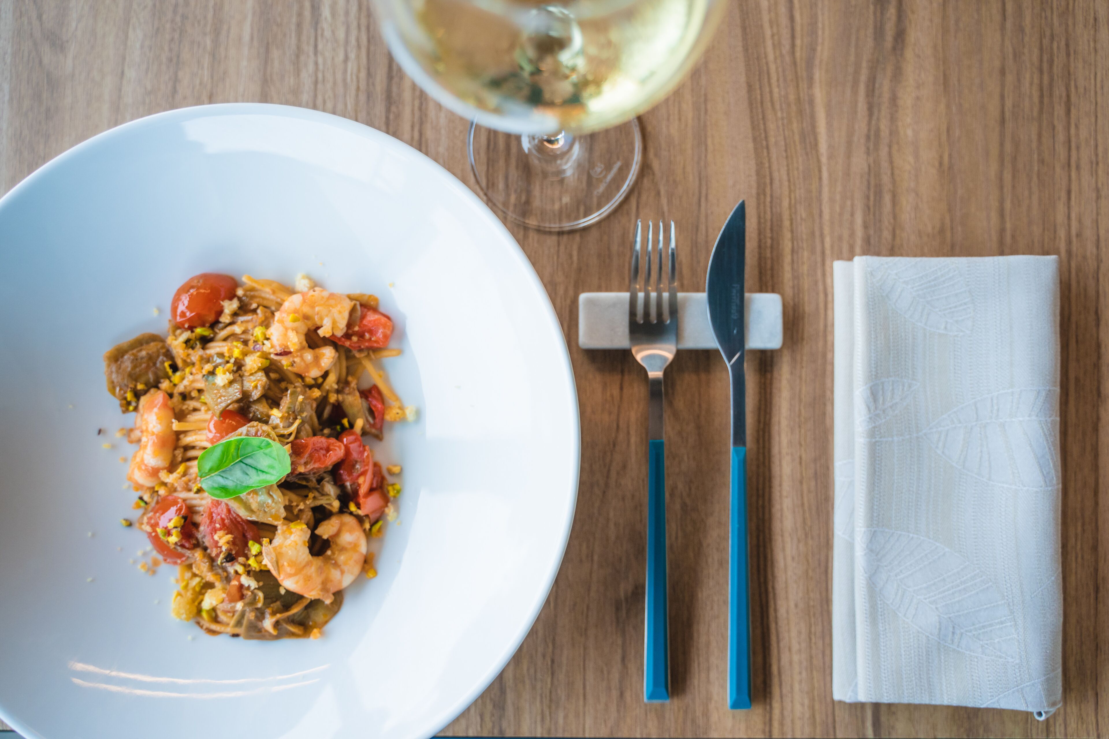 Un plato de pasta de mariscos blancos con una copa de vino blanco sobre una mesa de madera.