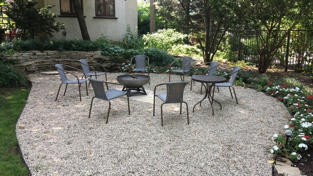 A patio area with outdoor furniture arranged around a fire pit, surrounded by gravel and greenery. - Sunny Coach House in Historic Oak Park (Oak Park)