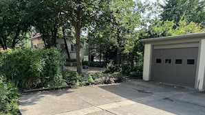A residential driveway with a garage, surrounded by trees and a garden. - Sunny Coach House in Historic Oak Park (Oak Park)
