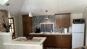 A modern kitchen with wooden cabinets, a white island, and a microwave. - Sunny Coach House in Historic Oak Park (Oak Park)